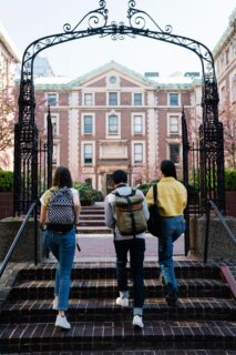 Three students entering college campus gate.